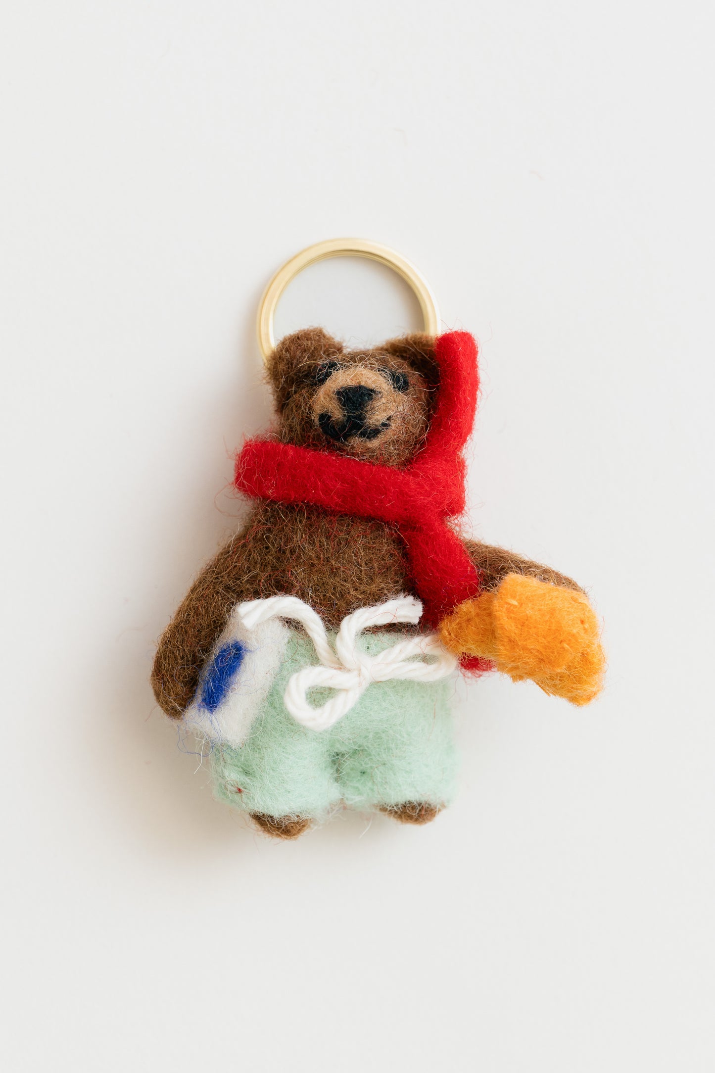 Felted teddy bear keychain with a red scarf and colorful bag on a white background