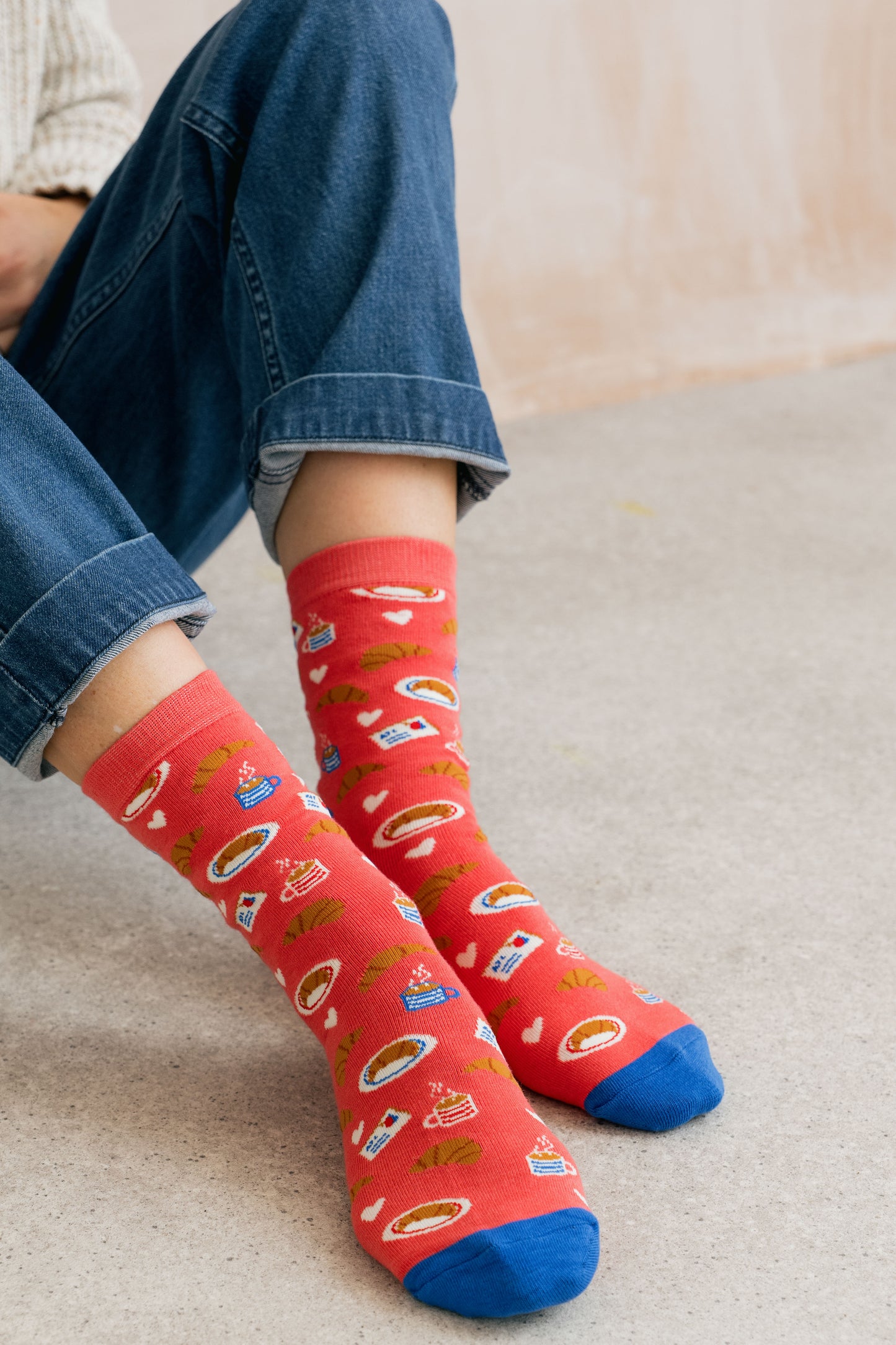 Red socks with colorful patterns worn by a person sitting on a beige surface.
