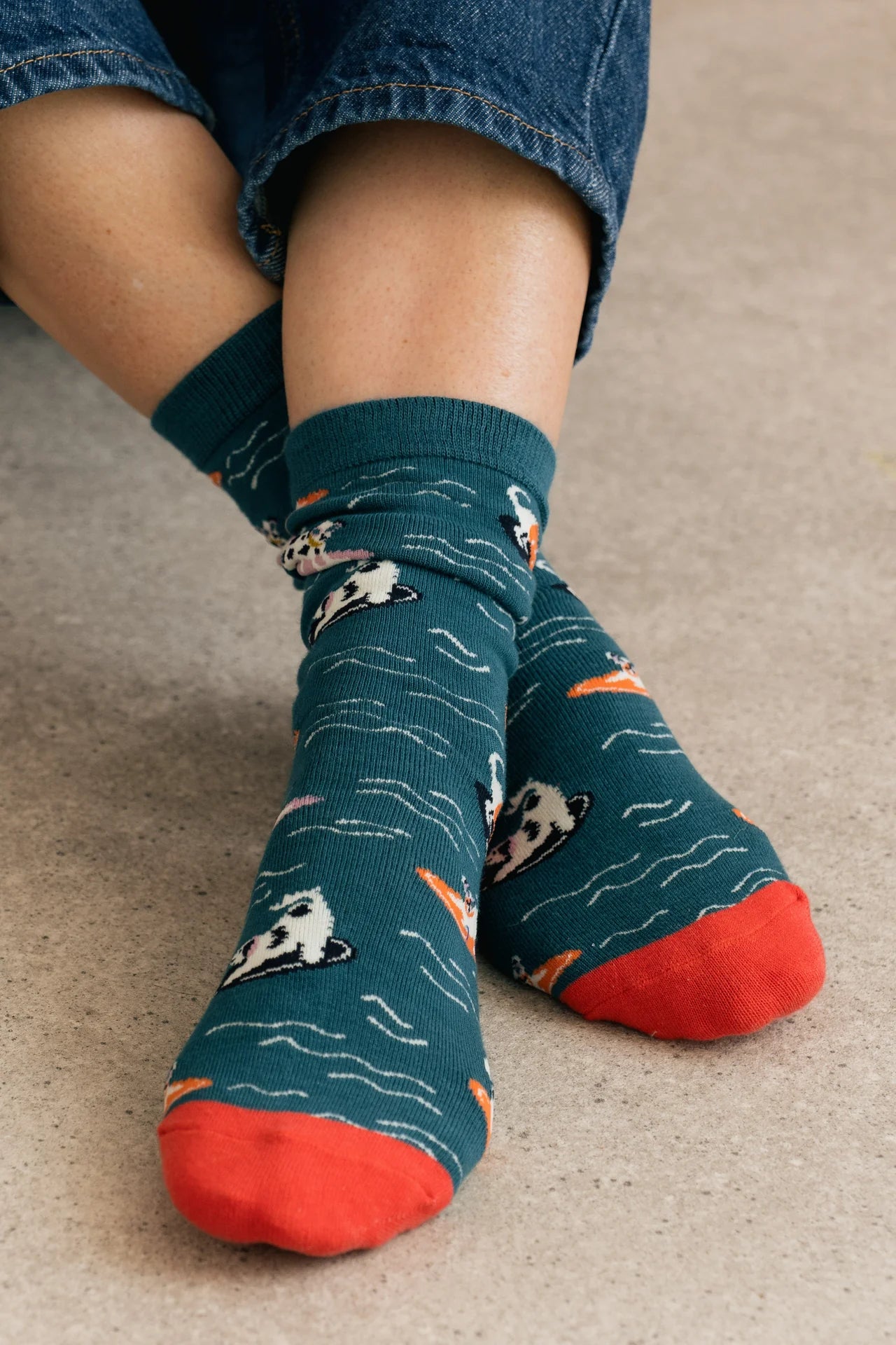 Person wearing blue socks with cat pattern and red toes on a beige floor.