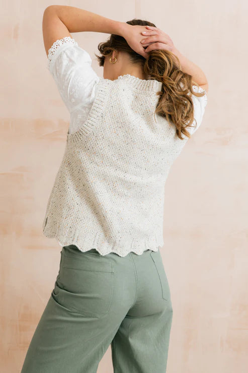 Woman wearing a white knit top and green pants against a pink background