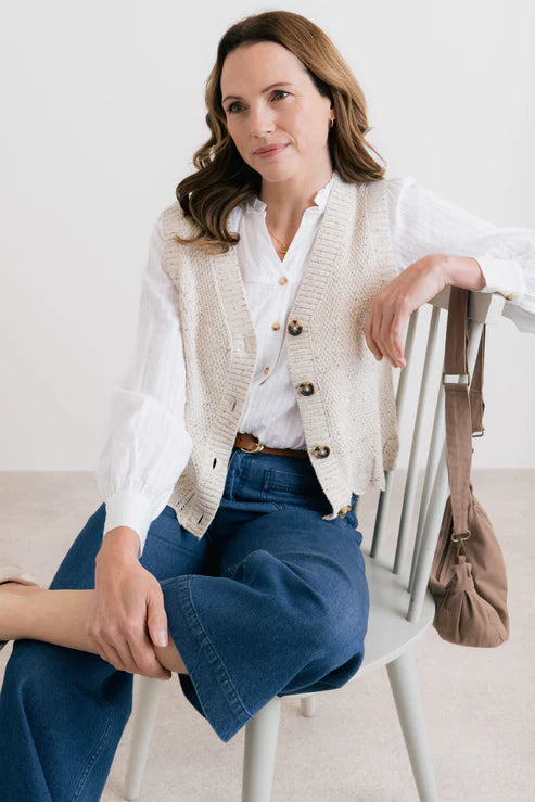 Woman sitting on a chair wearing a white shirt, beige cardigan, and blue jeans.