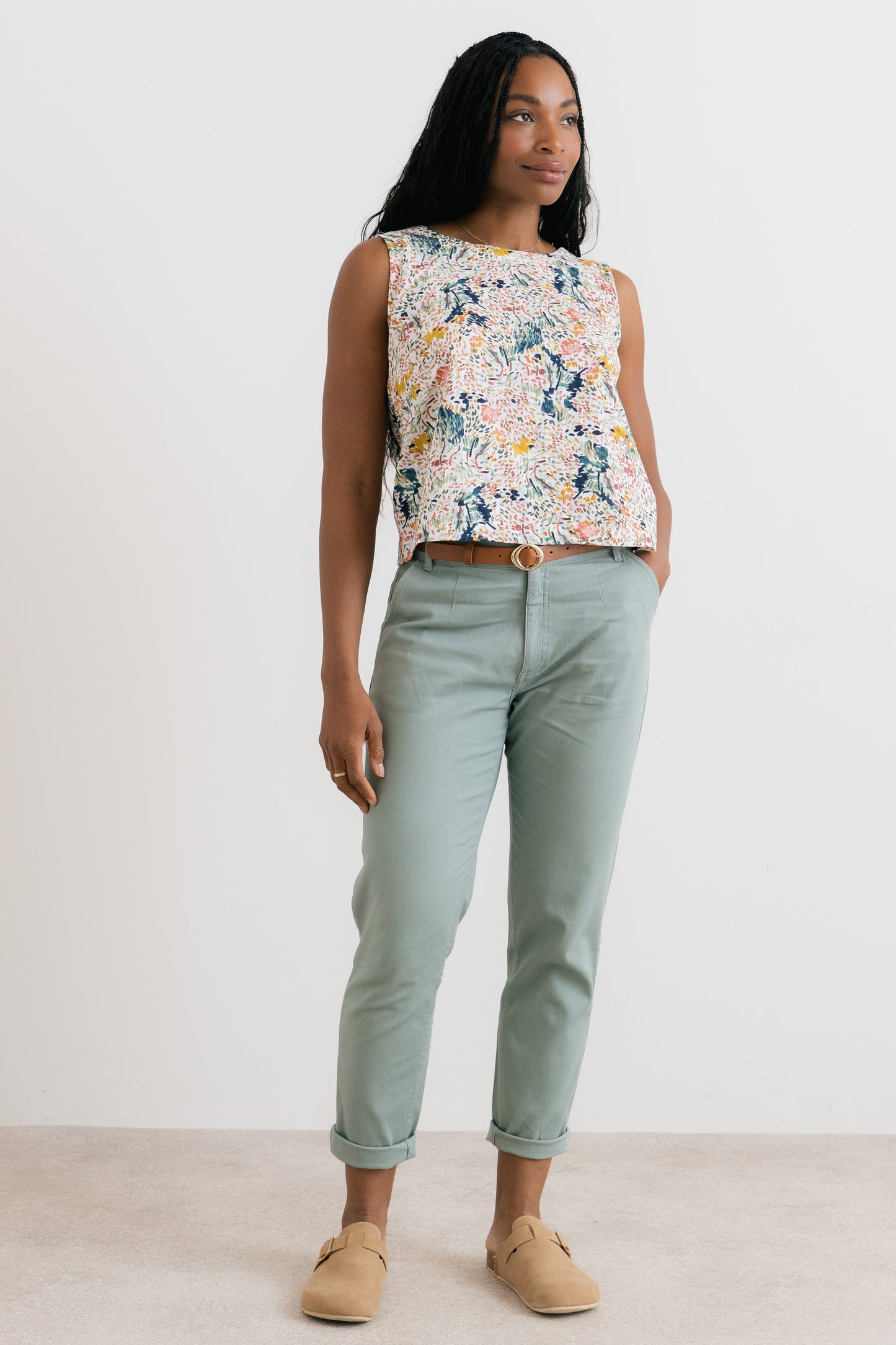 Woman wearing a floral sleeveless top and light blue pants against a white background