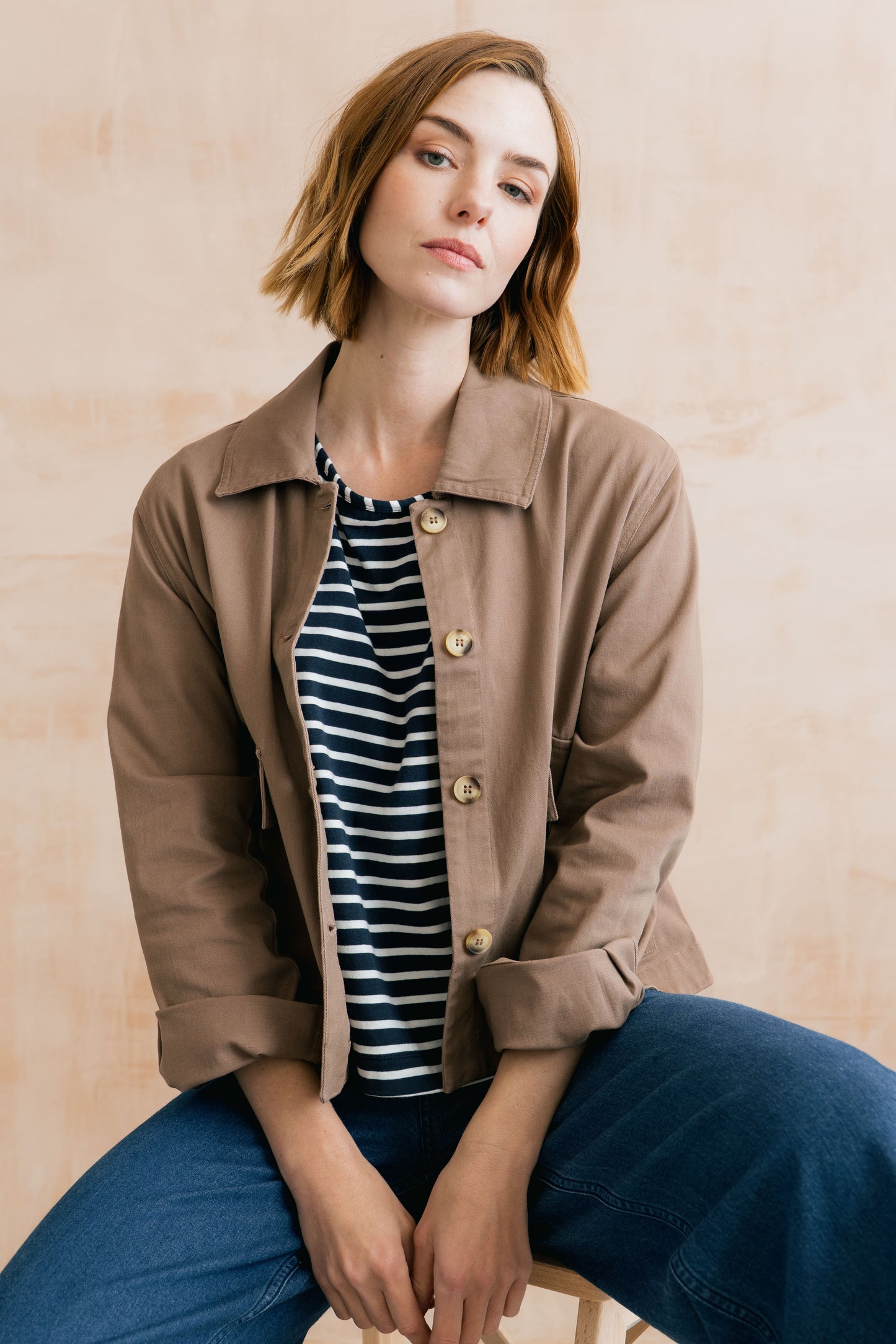 Woman wearing a brown jacket over a striped shirt with a beige background