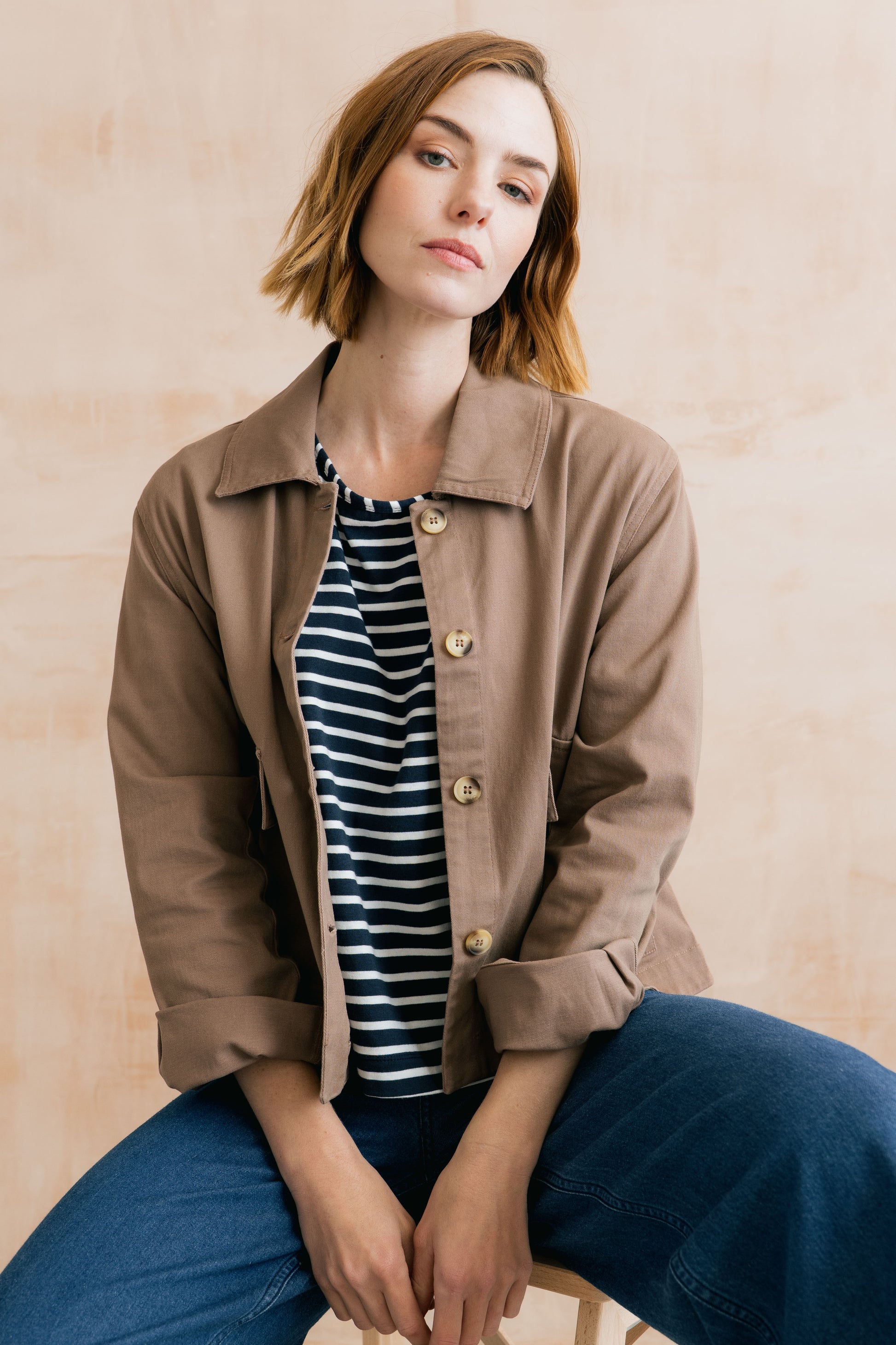 Woman wearing a brown jacket over a striped shirt with a beige background