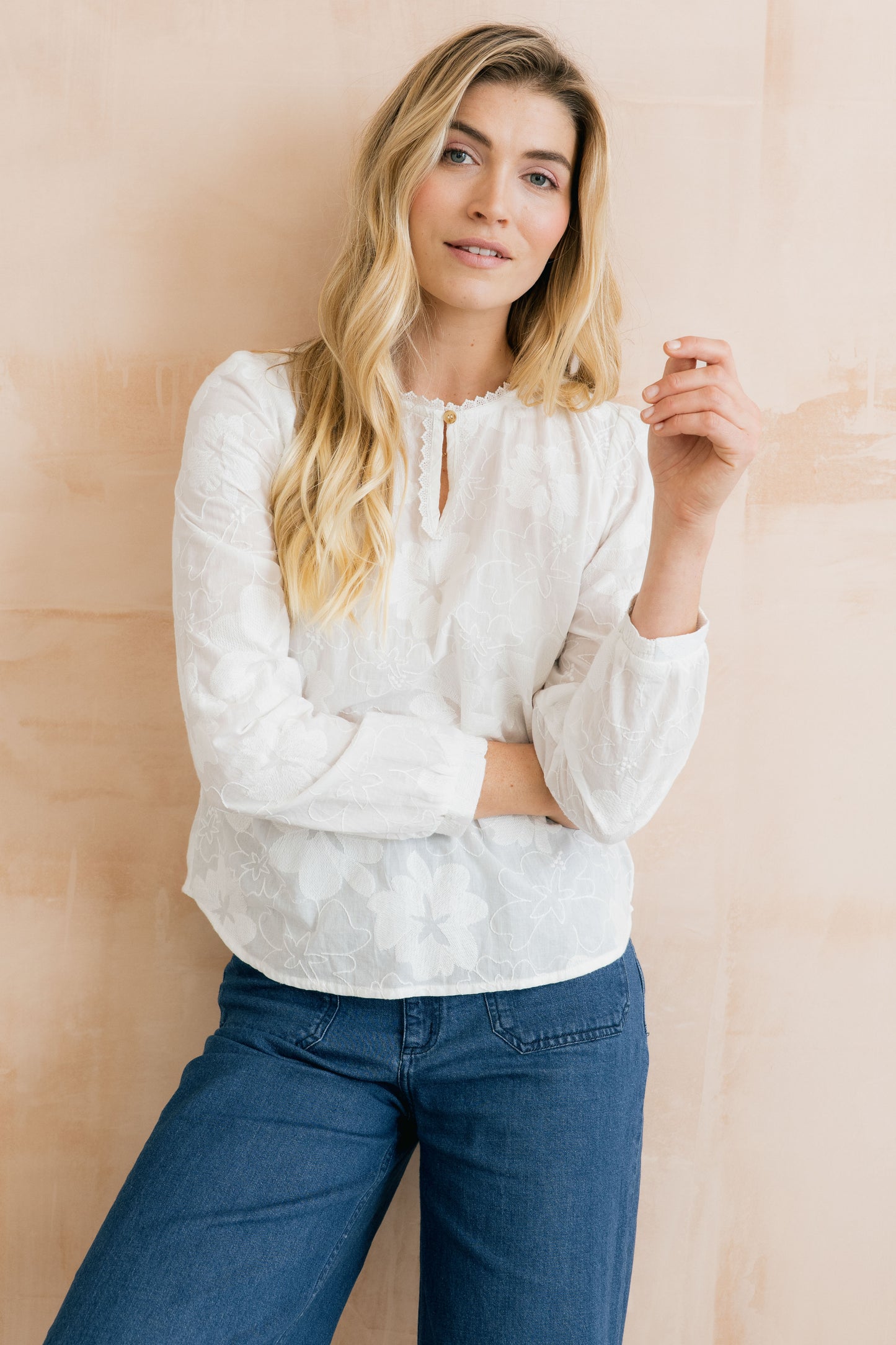 Woman wearing a white blouse and blue jeans against a beige background