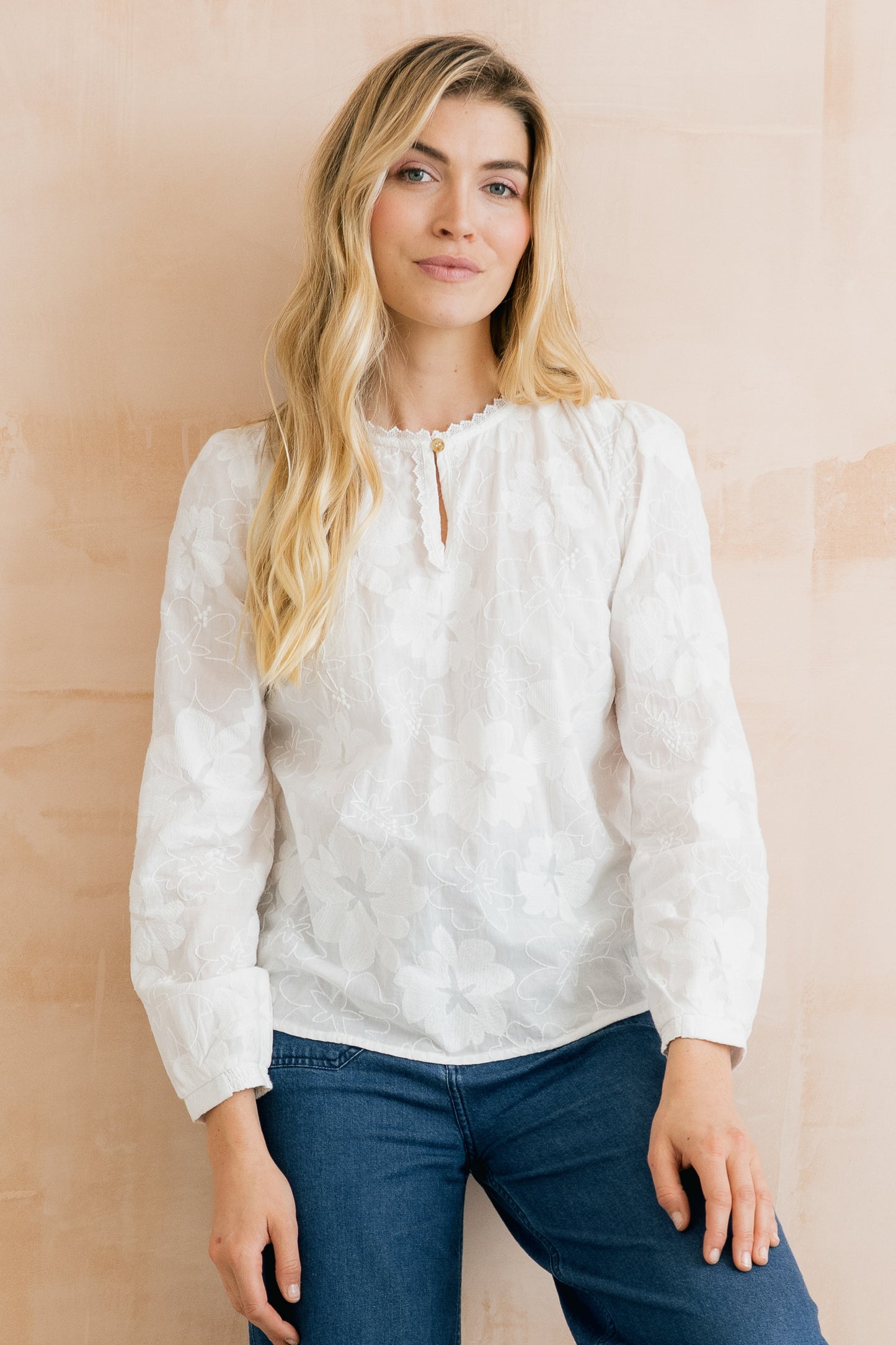 Woman wearing a white blouse with lace details against a beige background