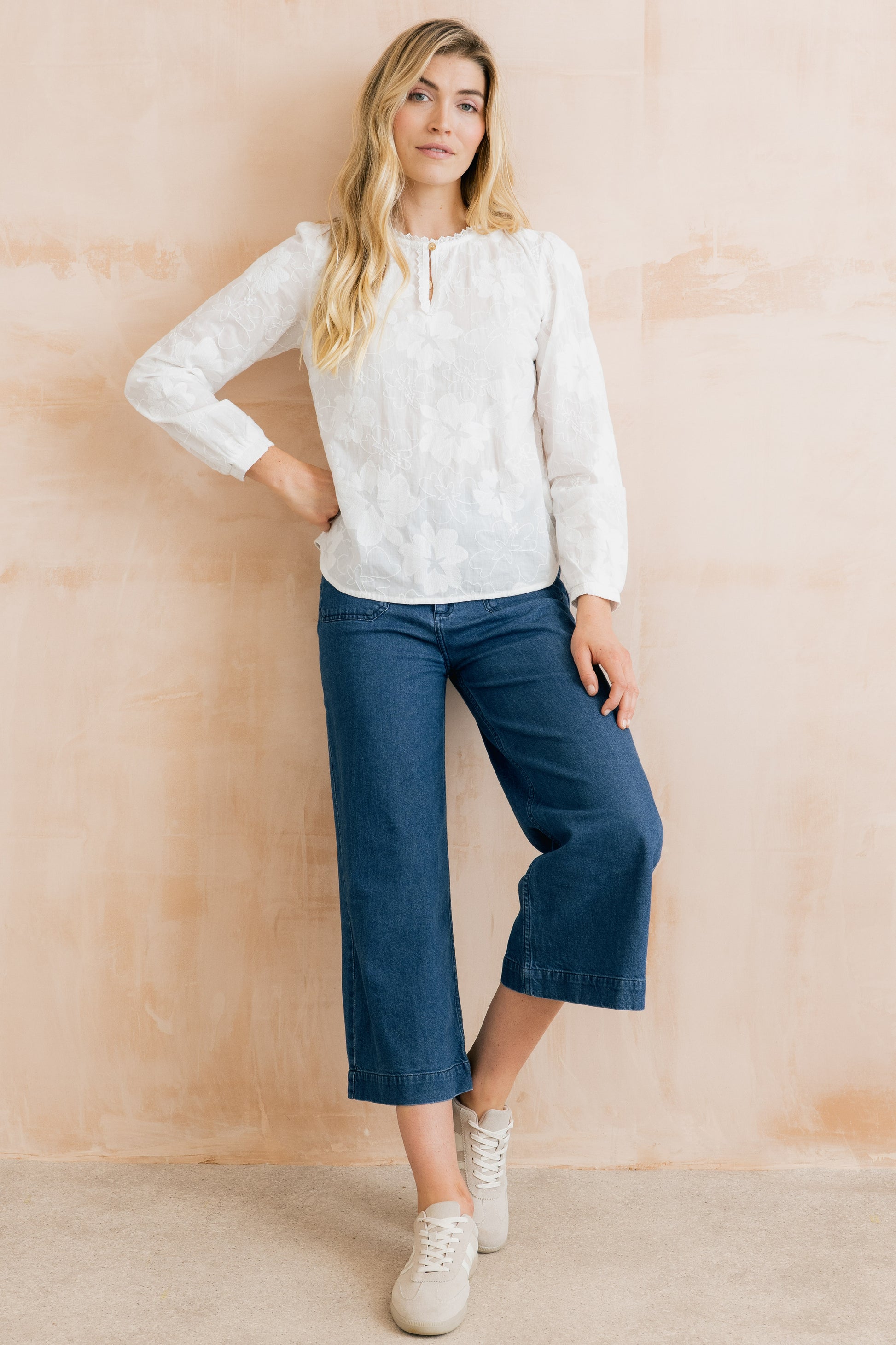 Woman wearing a white blouse and blue pants against a beige wall