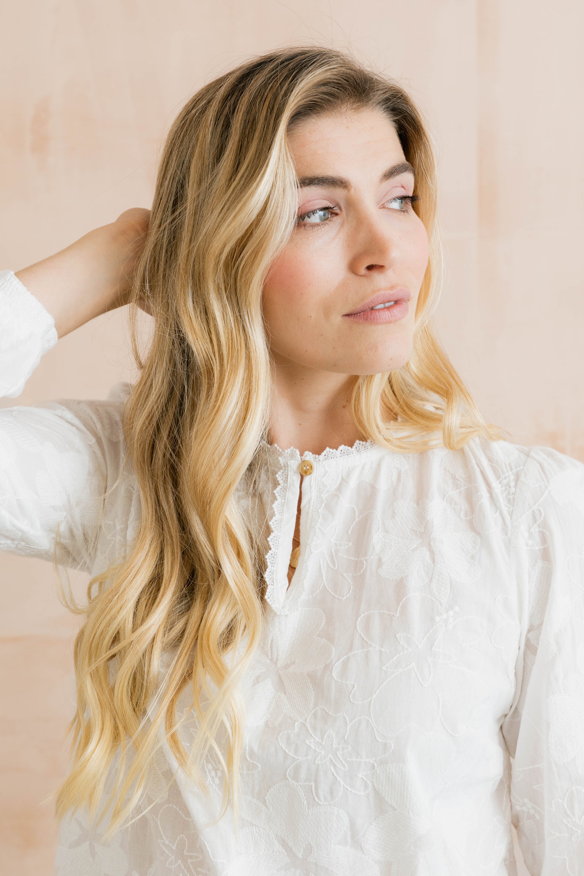 Woman with long blonde hair wearing a white blouse against a beige background