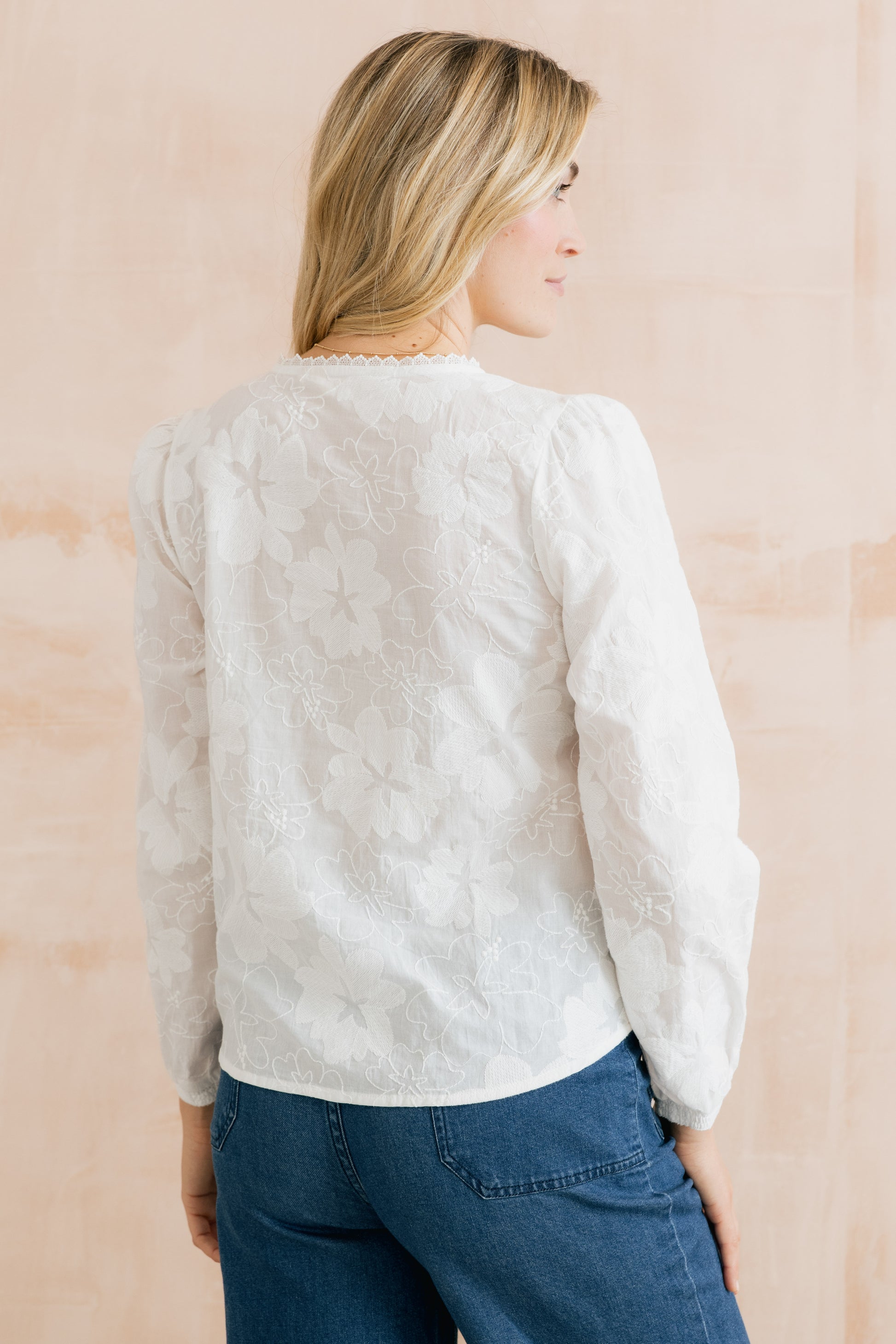 Woman wearing a white textured sweater and blue jeans against a beige background
