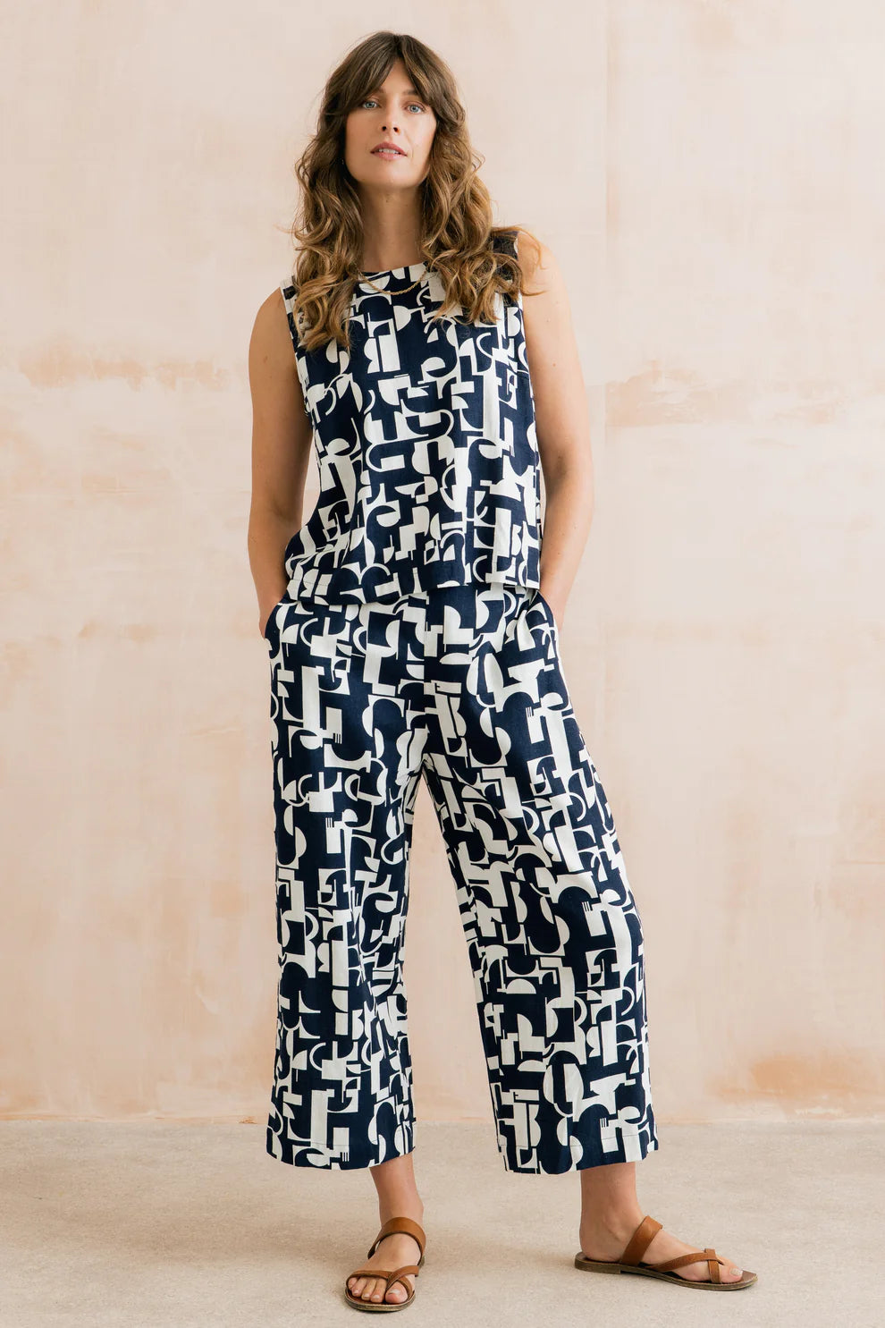 Woman wearing a sleeveless jumpsuit with geometric pattern against a beige background