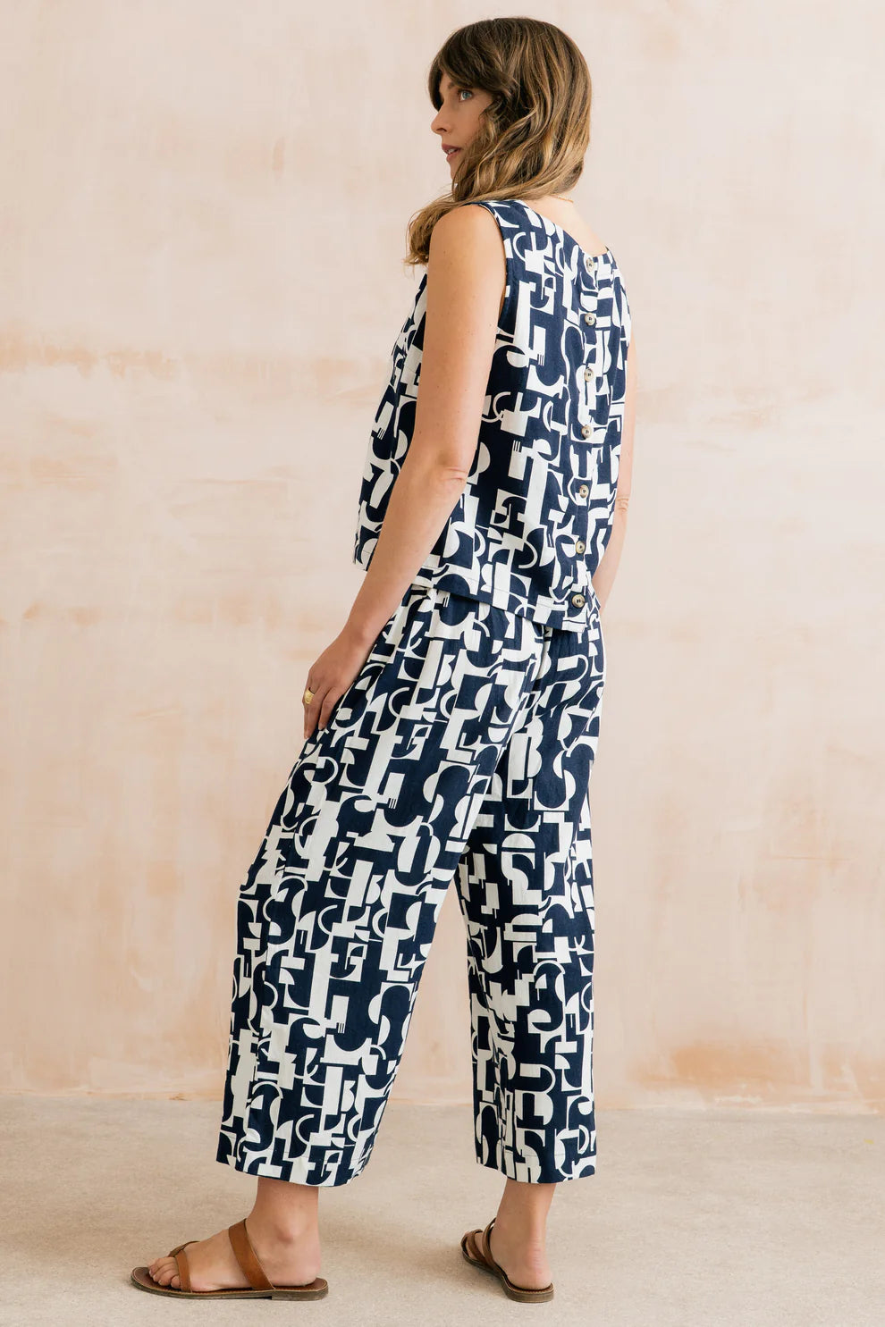 Woman wearing a sleeveless jumpsuit with a geometric pattern against a plain background