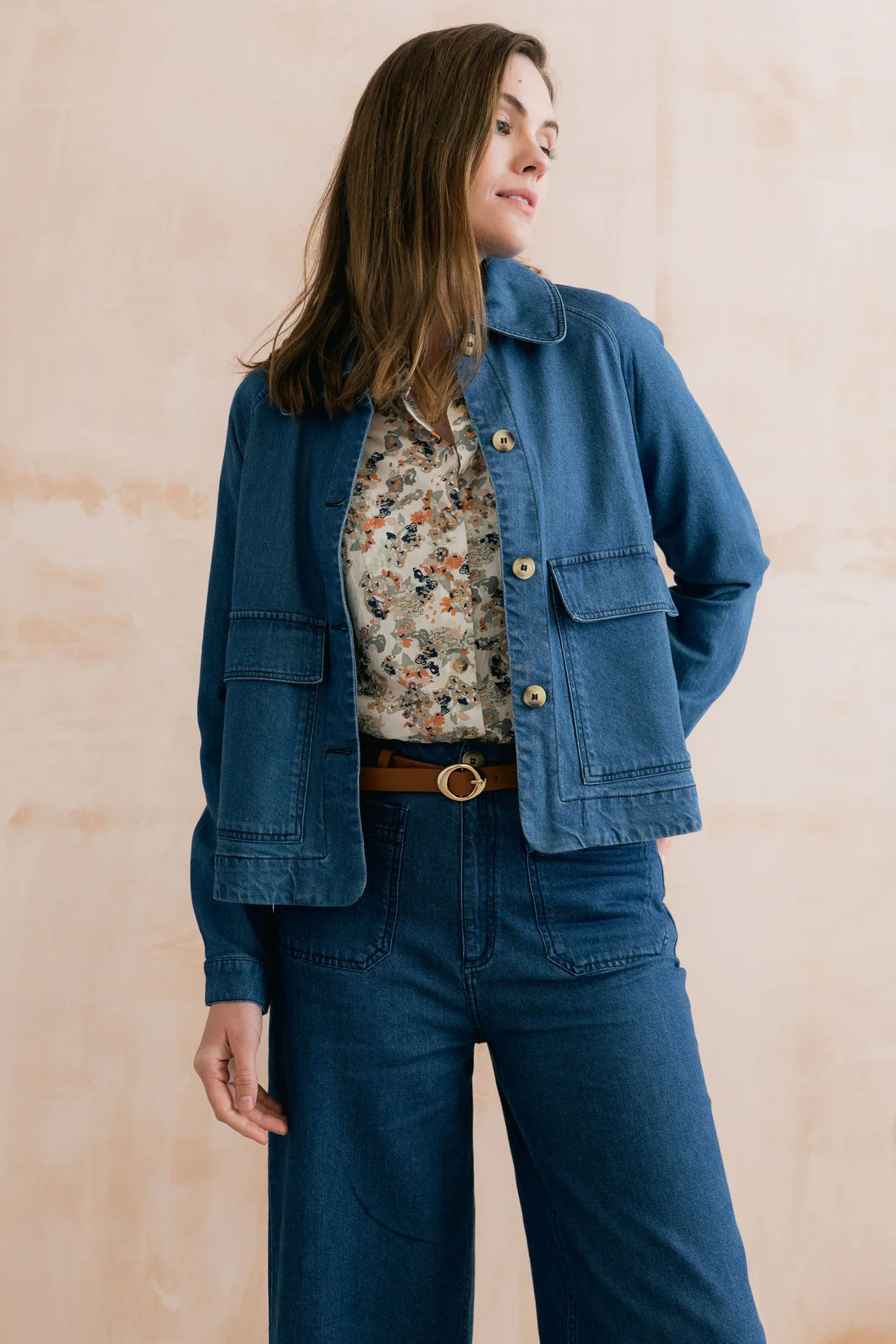Woman wearing a blue denim jacket and jeans against a beige background