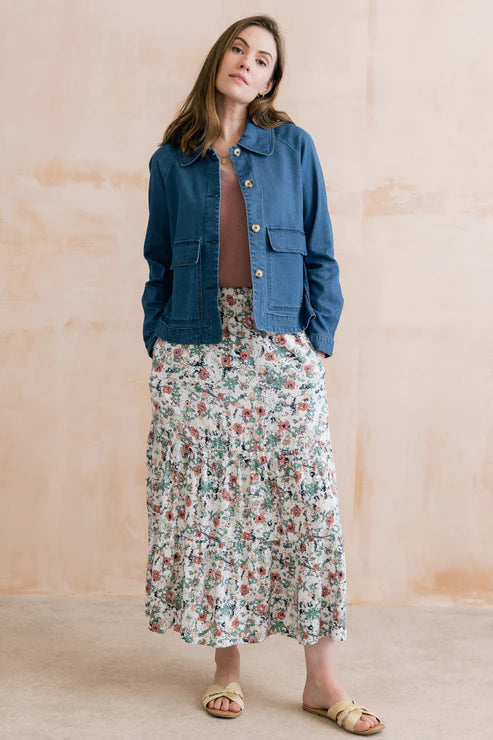 Woman wearing a blue denim jacket and floral skirt against a beige background