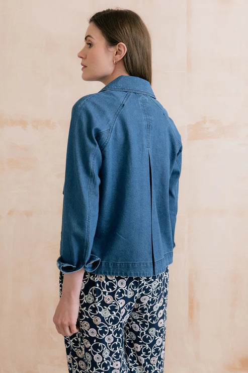 Woman wearing a blue denim jacket and floral pants against a beige background