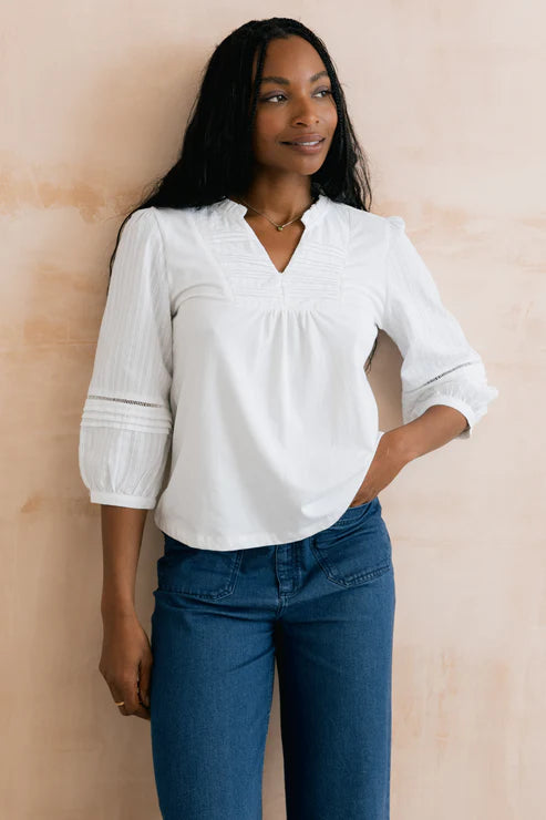 Woman wearing a white blouse and blue jeans against a beige wall