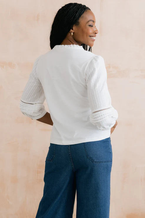 Woman wearing a light gray sweater and blue jeans against a beige background