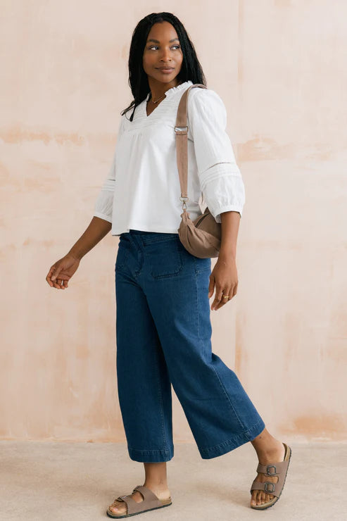 Woman wearing a white blouse and blue pants with a beige bag against a light background