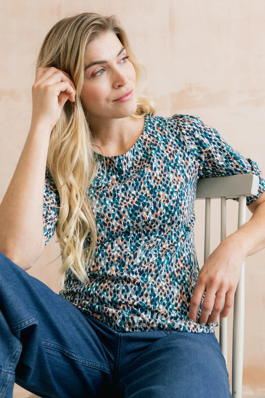 Woman wearing a patterned shirt sitting on a chair with a neutral background