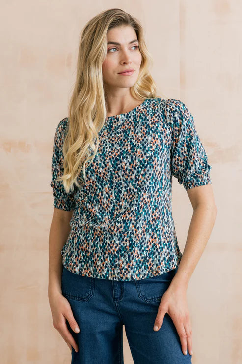 Woman wearing a patterned top and blue jeans against a beige background