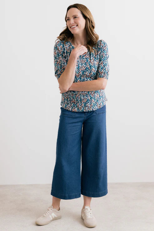 Woman wearing a patterned top and blue pants on a white background