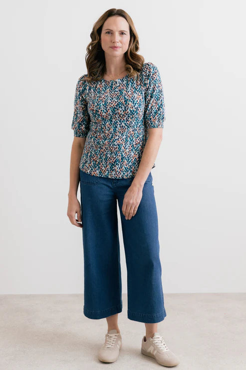 Woman wearing a patterned top and blue jeans against a white background