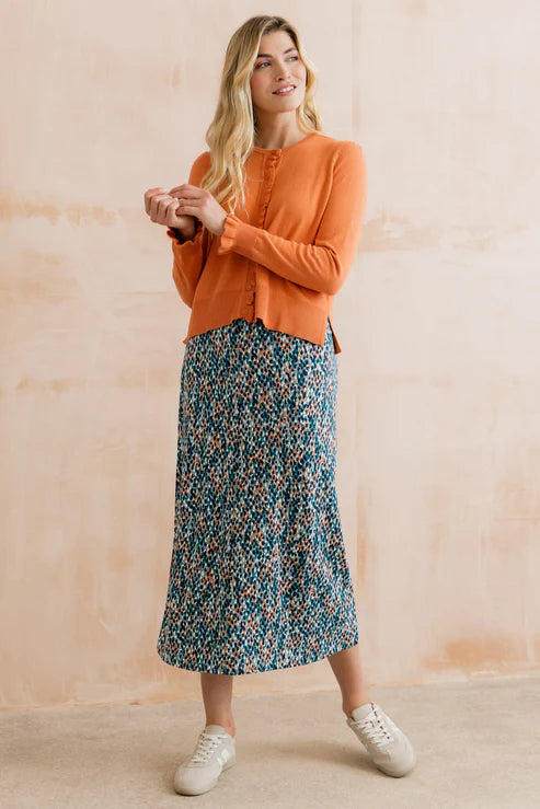 Woman wearing an orange cardigan and floral skirt against a beige background