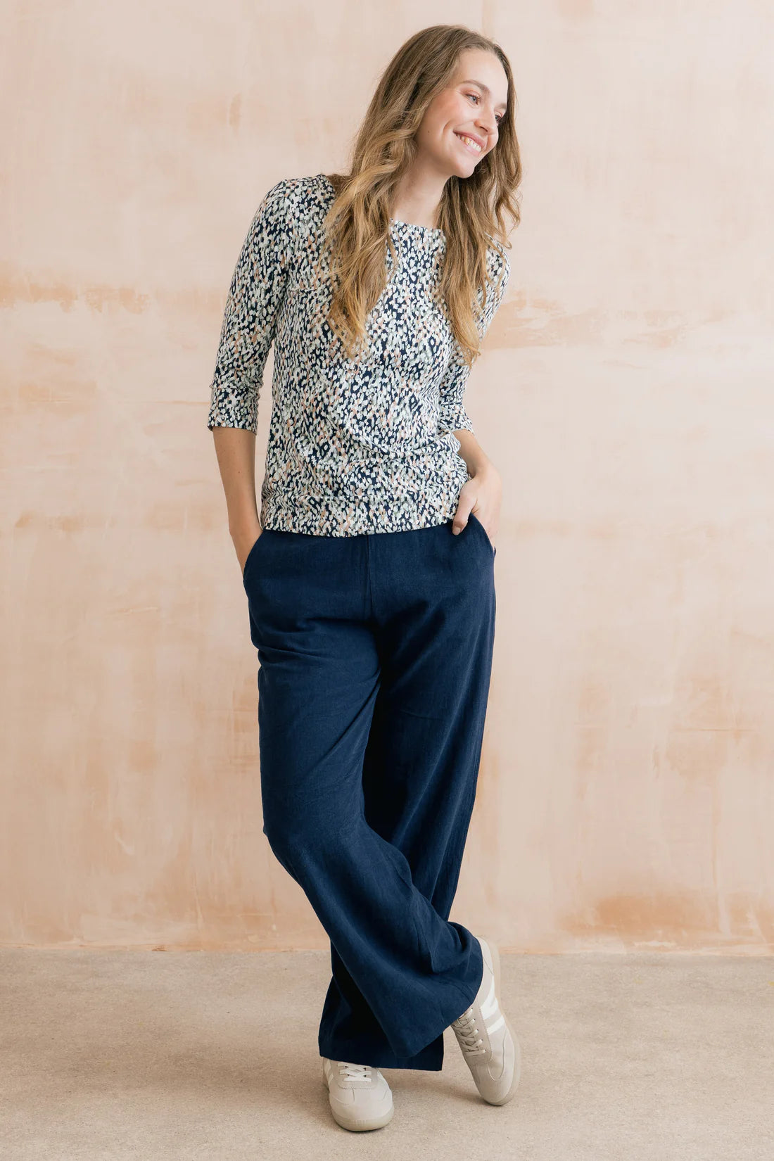 Woman wearing a patterned top and navy pants against a beige wall
