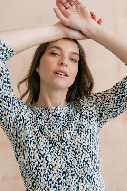Woman wearing a patterned top with her arms raised against a beige background