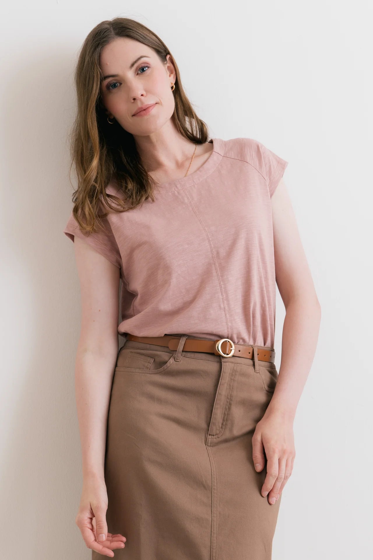 Woman wearing a pink top and brown pants against a plain background