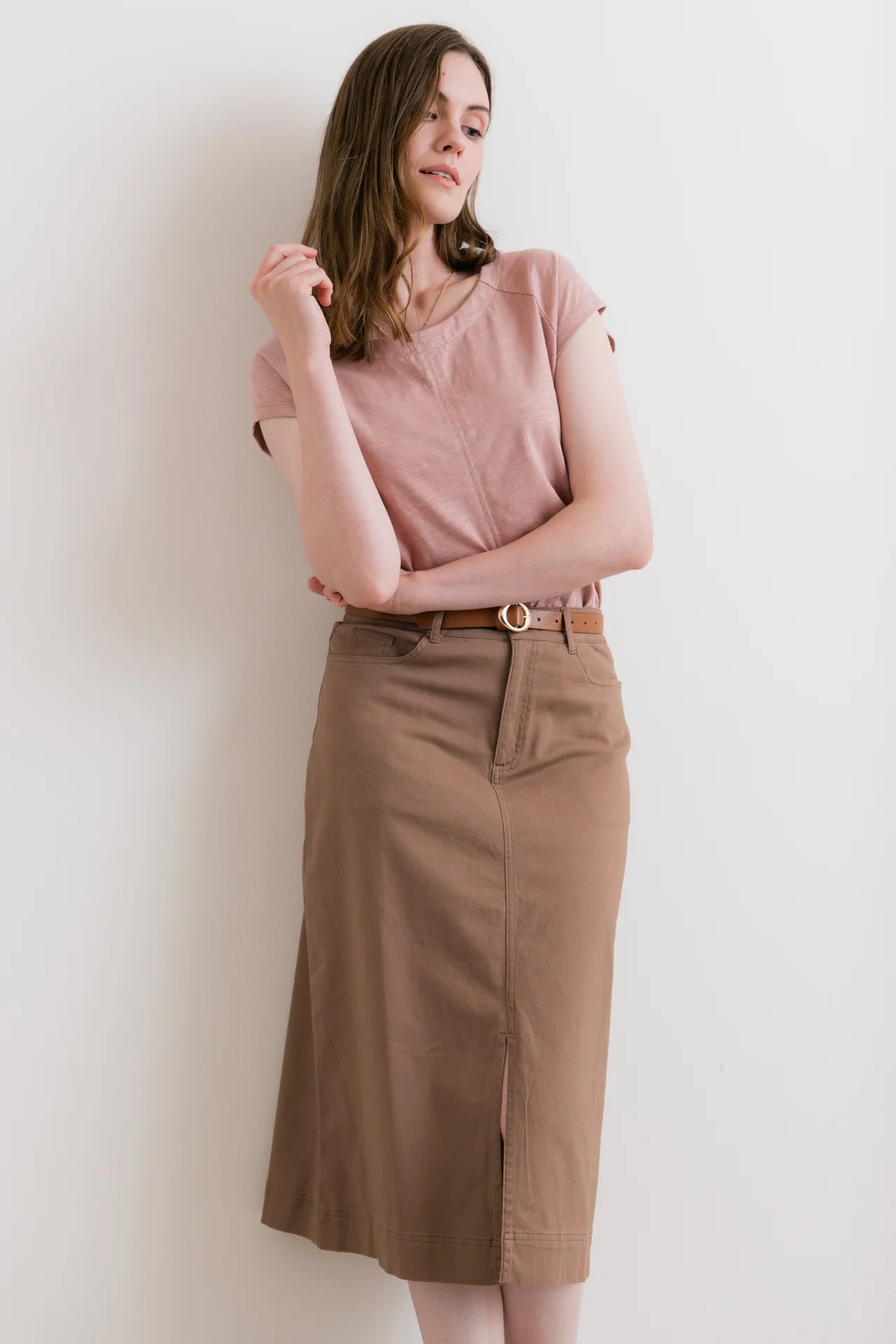 Woman wearing a pink top and brown skirt against a white background