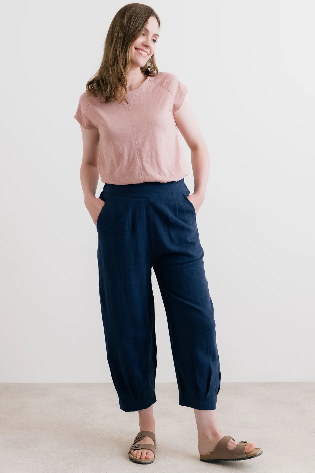 Woman wearing a pink sleeveless top and navy pants against a white background