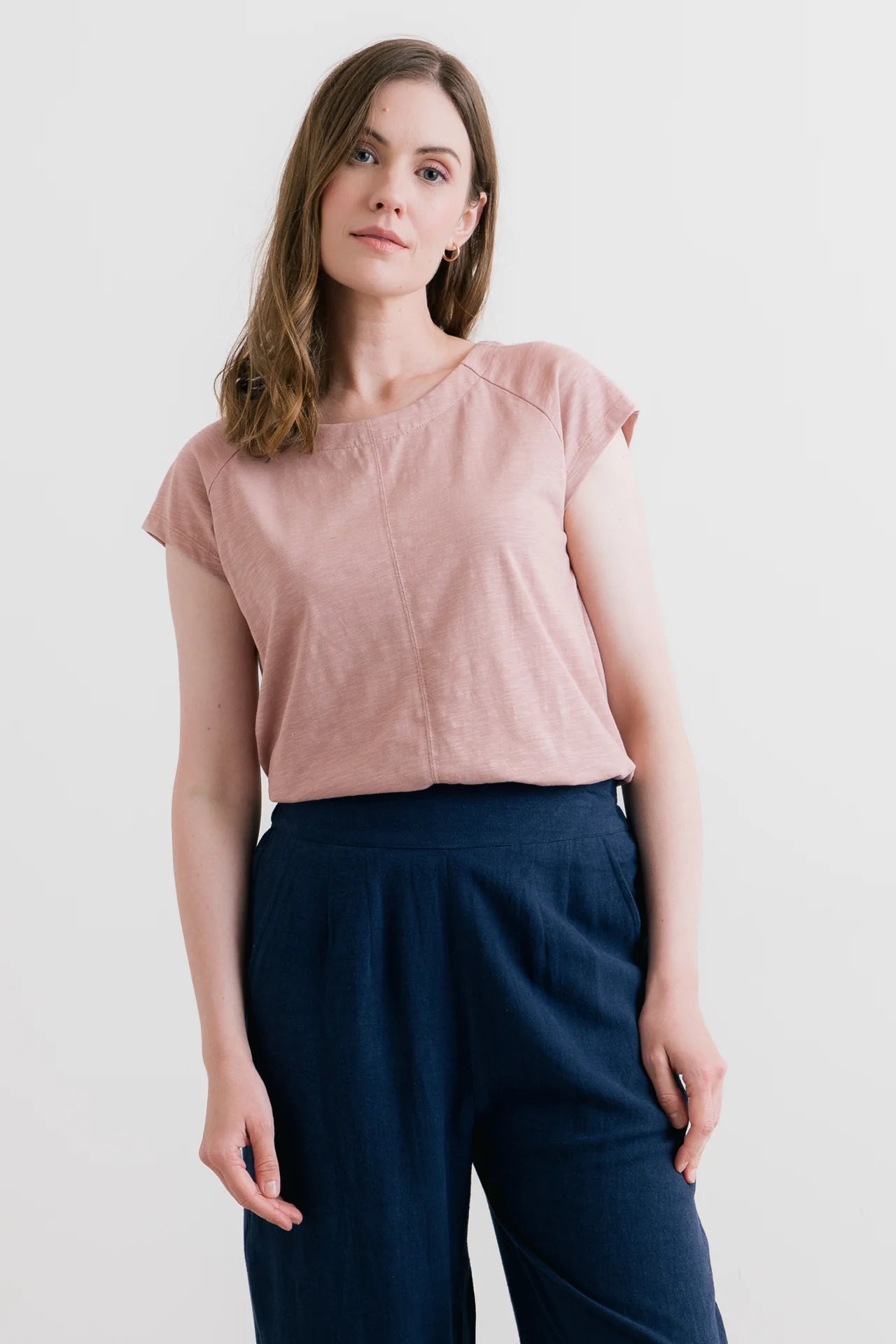Woman wearing a pink top and navy pants against a white background