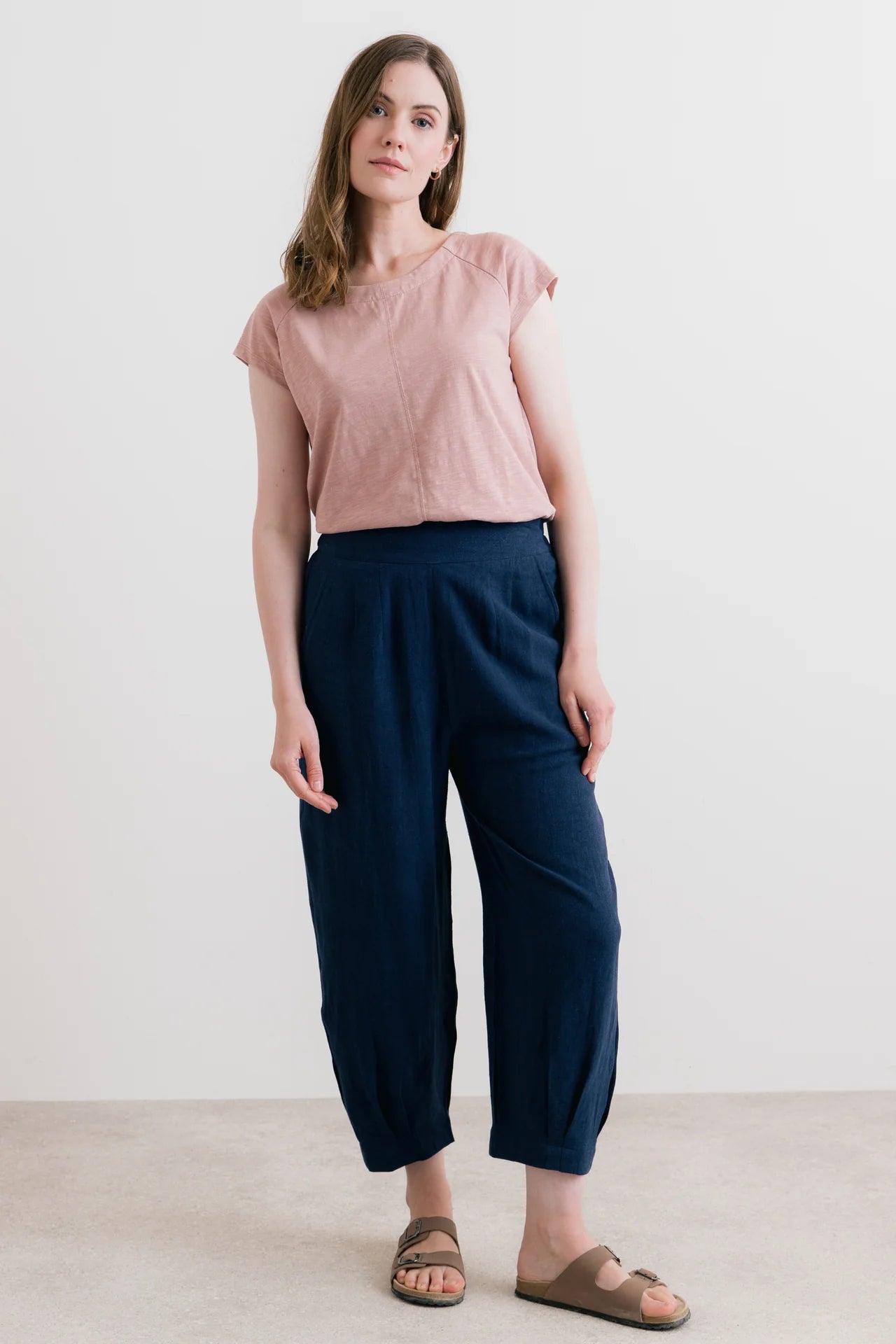 Woman wearing a pink top and navy pants against a white background