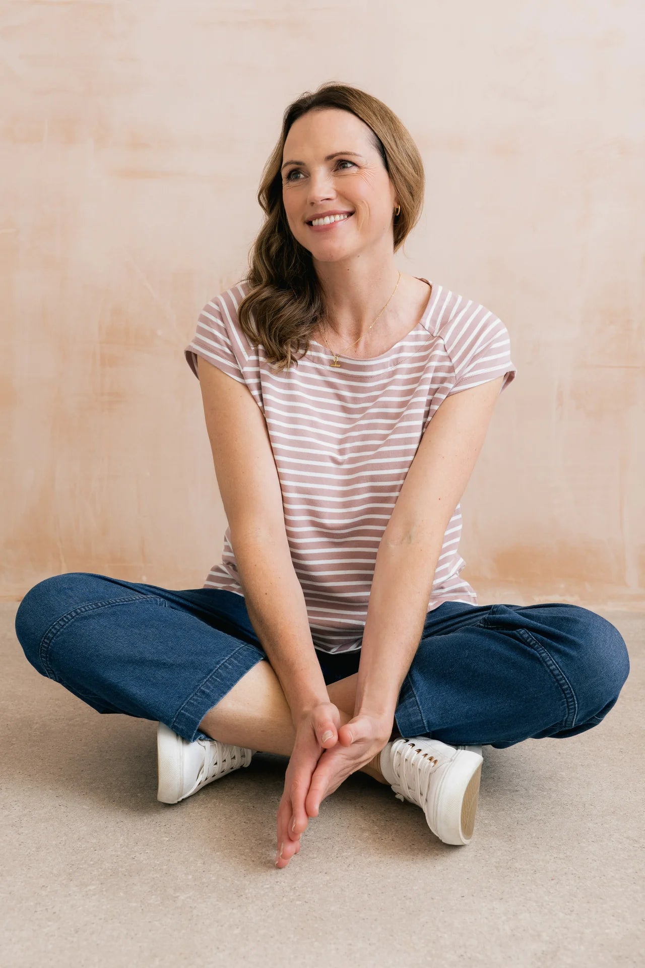 Woman sitting cross-legged on a beige floor with a neutral background