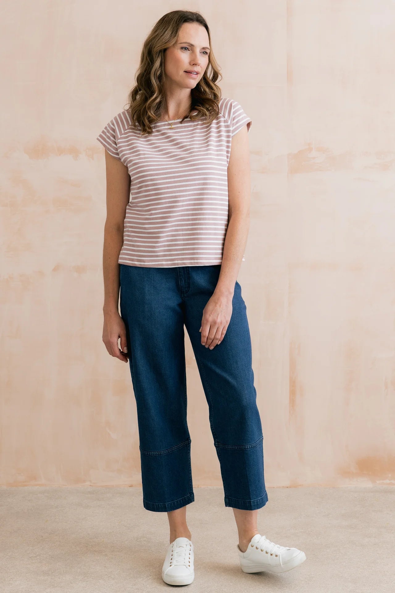 Woman wearing a striped shirt and blue pants against a beige wall