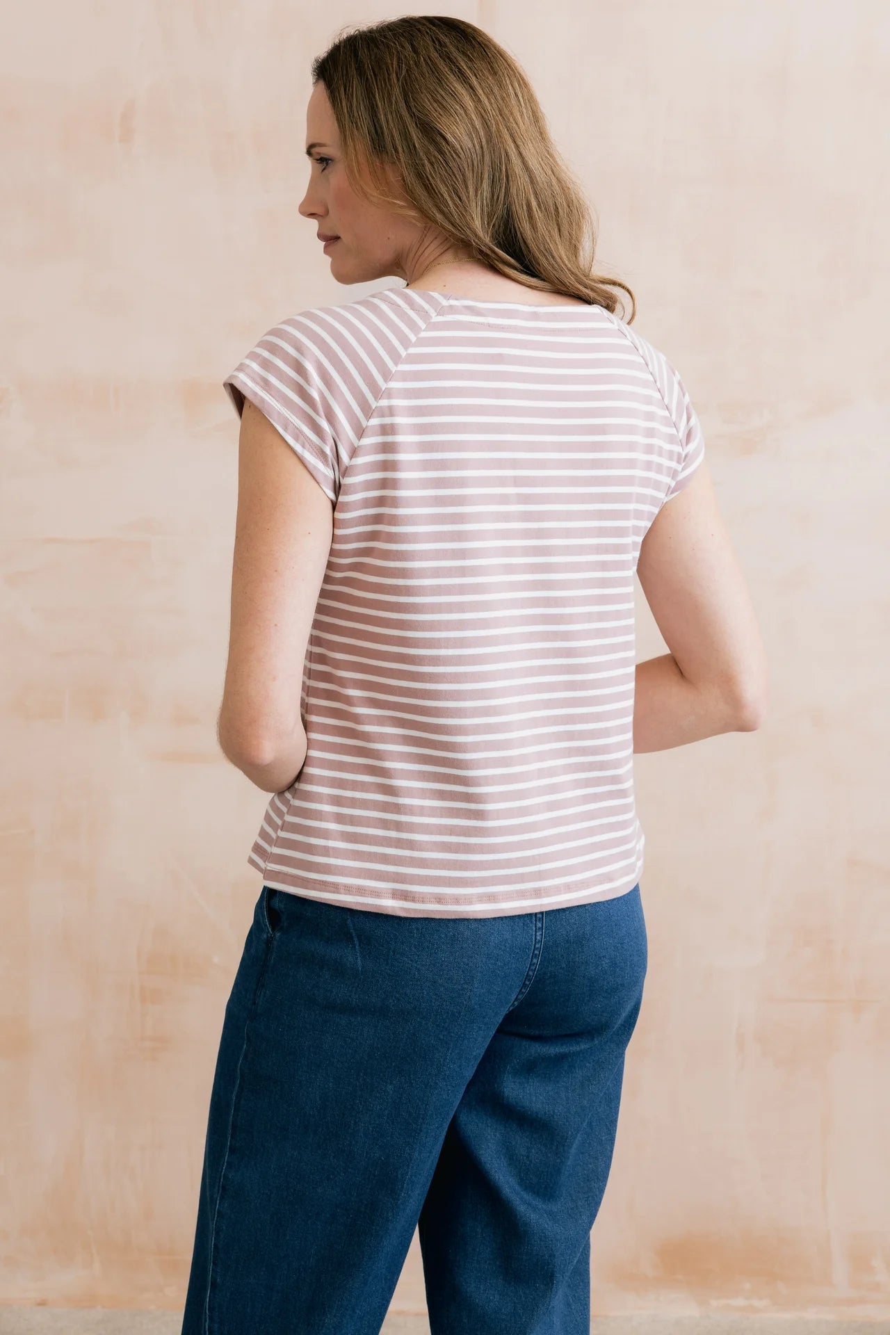 Woman wearing a striped shirt and blue pants against a beige wall