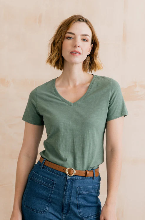 Woman wearing a green t-shirt and blue jeans against a beige background