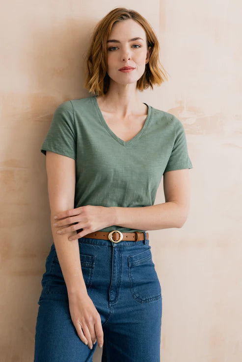 Woman wearing a green t-shirt and blue jeans against a beige wall