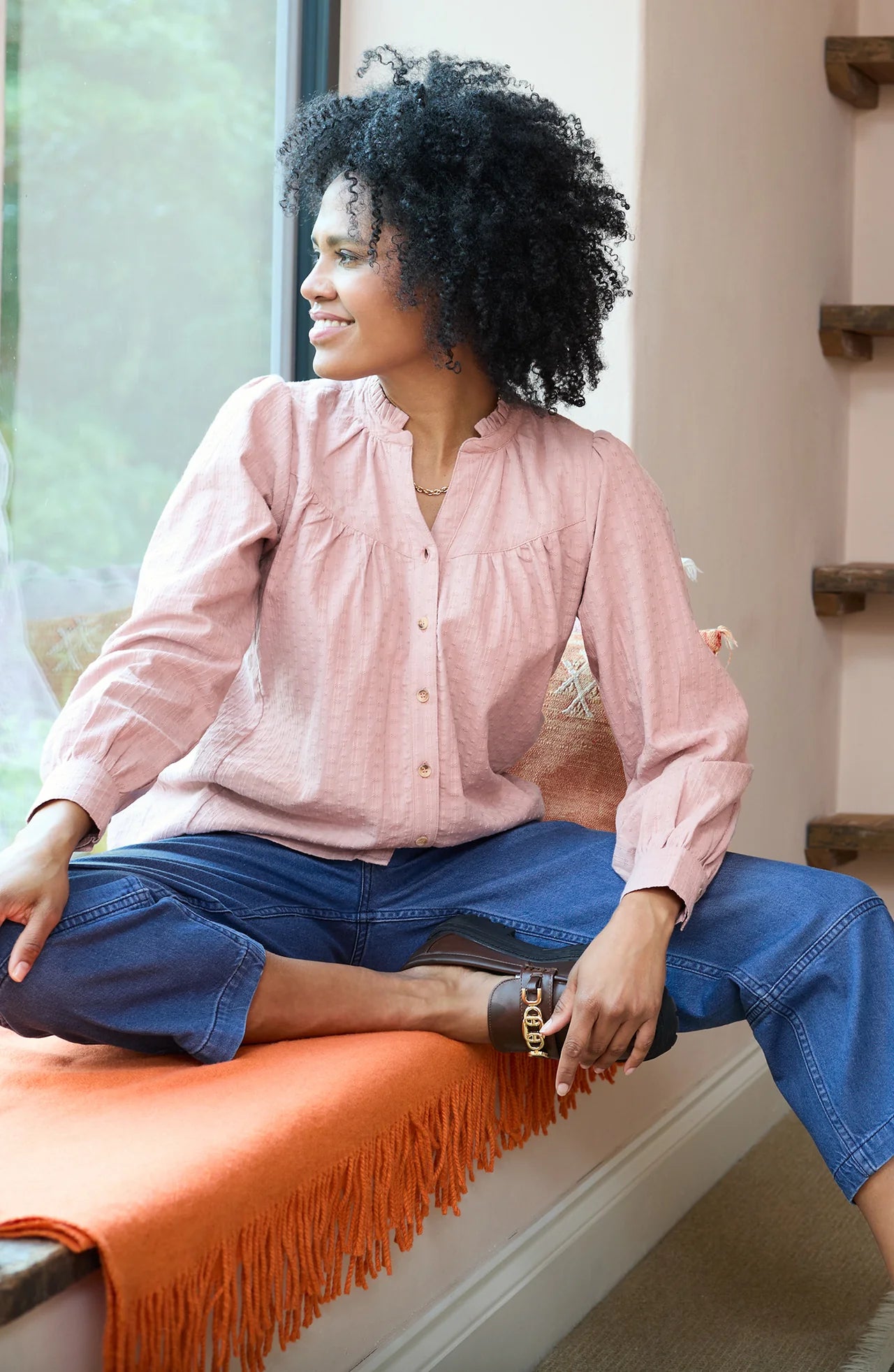 Woman sitting on an orange bench wearing a pink blouse and blue pants.