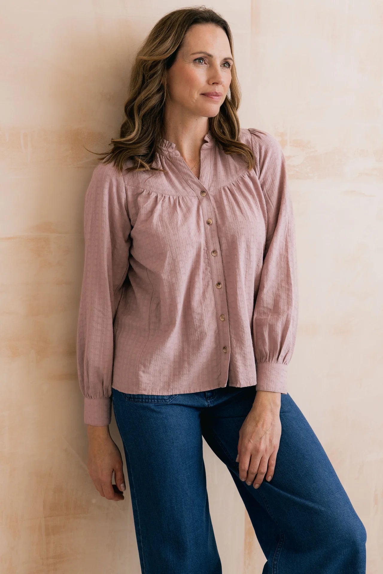 Woman wearing a pink blouse and blue jeans against a beige wall