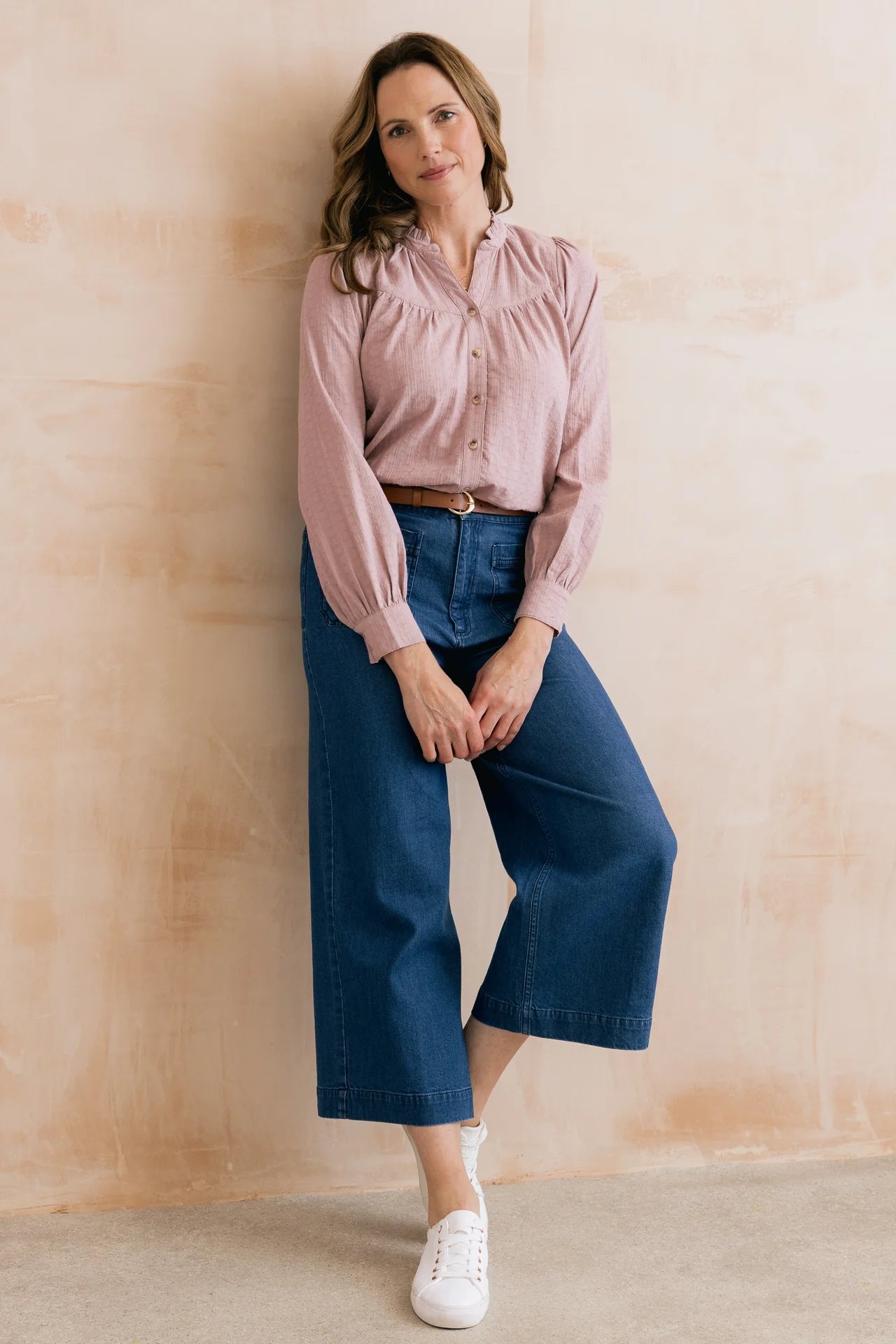 Woman wearing a pink blouse and blue jeans against a beige wall