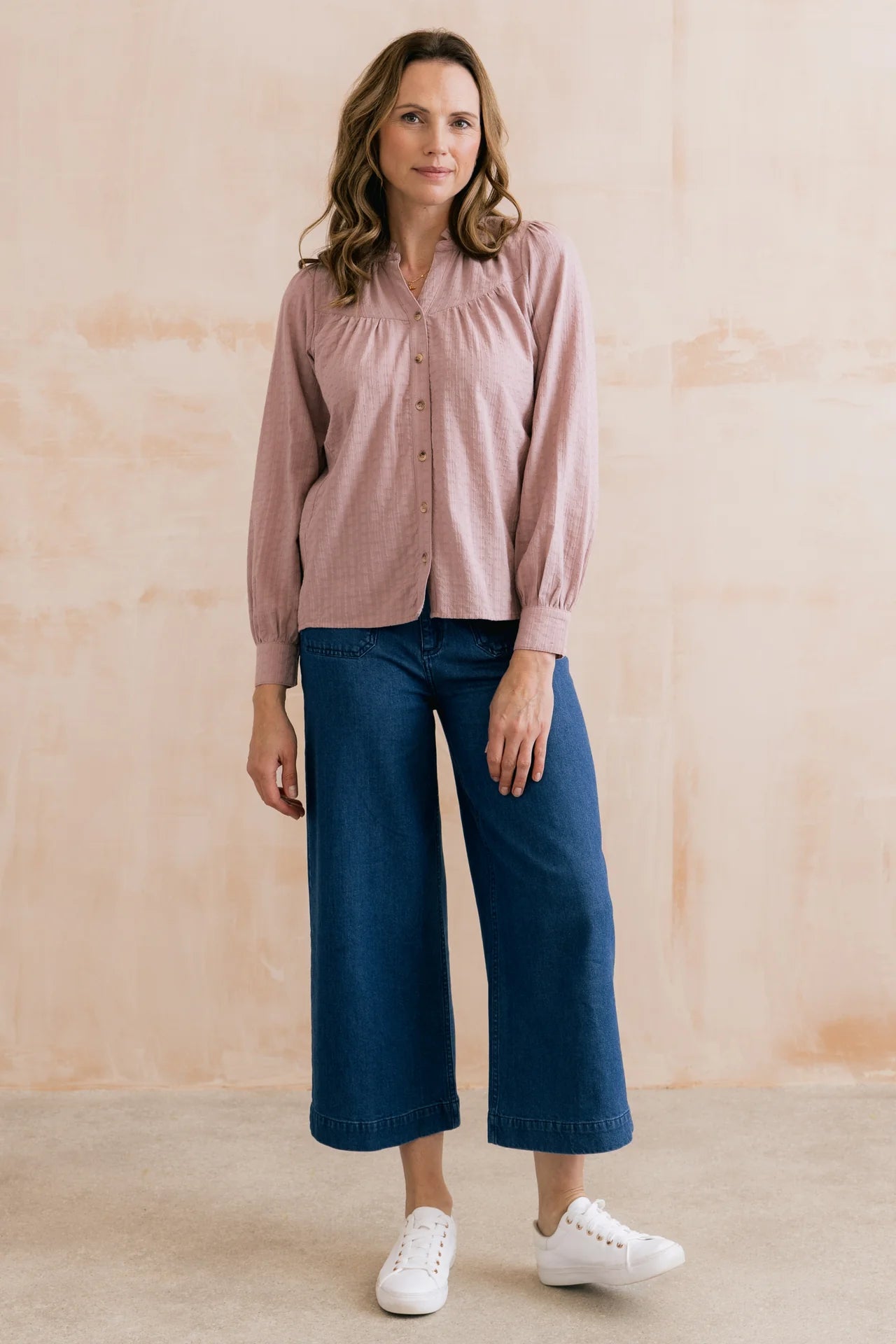 Woman wearing a pink shirt and blue jeans against a beige background