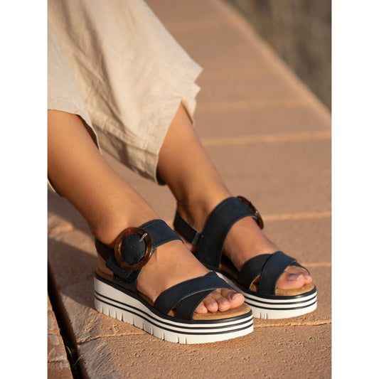 Navy sandals with white soles worn by a person sitting on a stone surface.