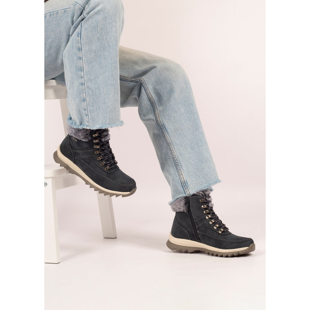 Person wearing black winter boots with fur-lined cuffs, sitting on a white stool against a light background.