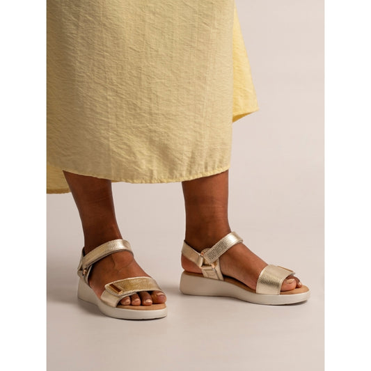 Gold sandals worn with a yellow skirt on a neutral background