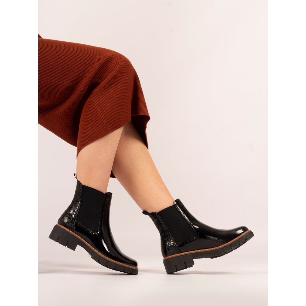 Black glossy boots worn with a rust-colored skirt on a light background