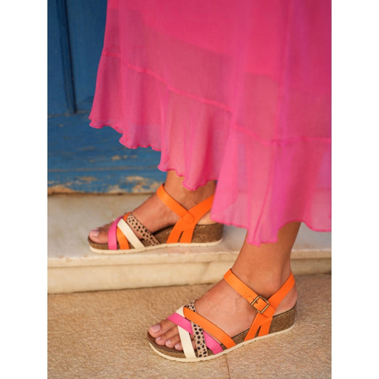 Orange sandals worn with a pink skirt on a neutral background