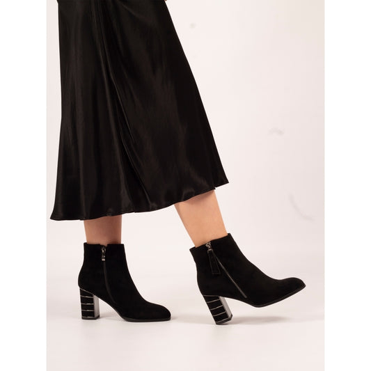 Black ankle boots worn with a black skirt on a white background