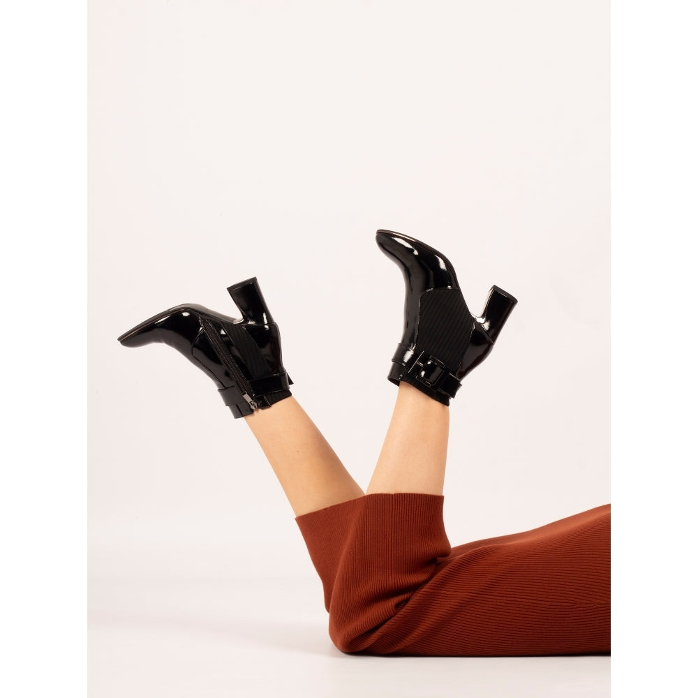 Black patent leather boots worn with brown pants on a white background