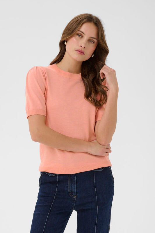 Woman wearing a pink top and dark jeans on a white background
